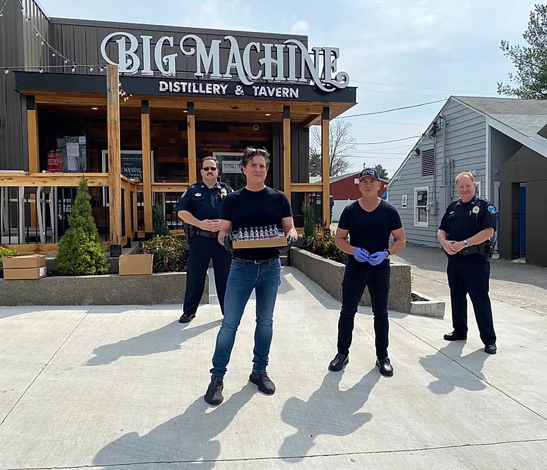 Scott Borchetta holds the case of hand sanitizer while his brother Mark and Nashville's Finest look on