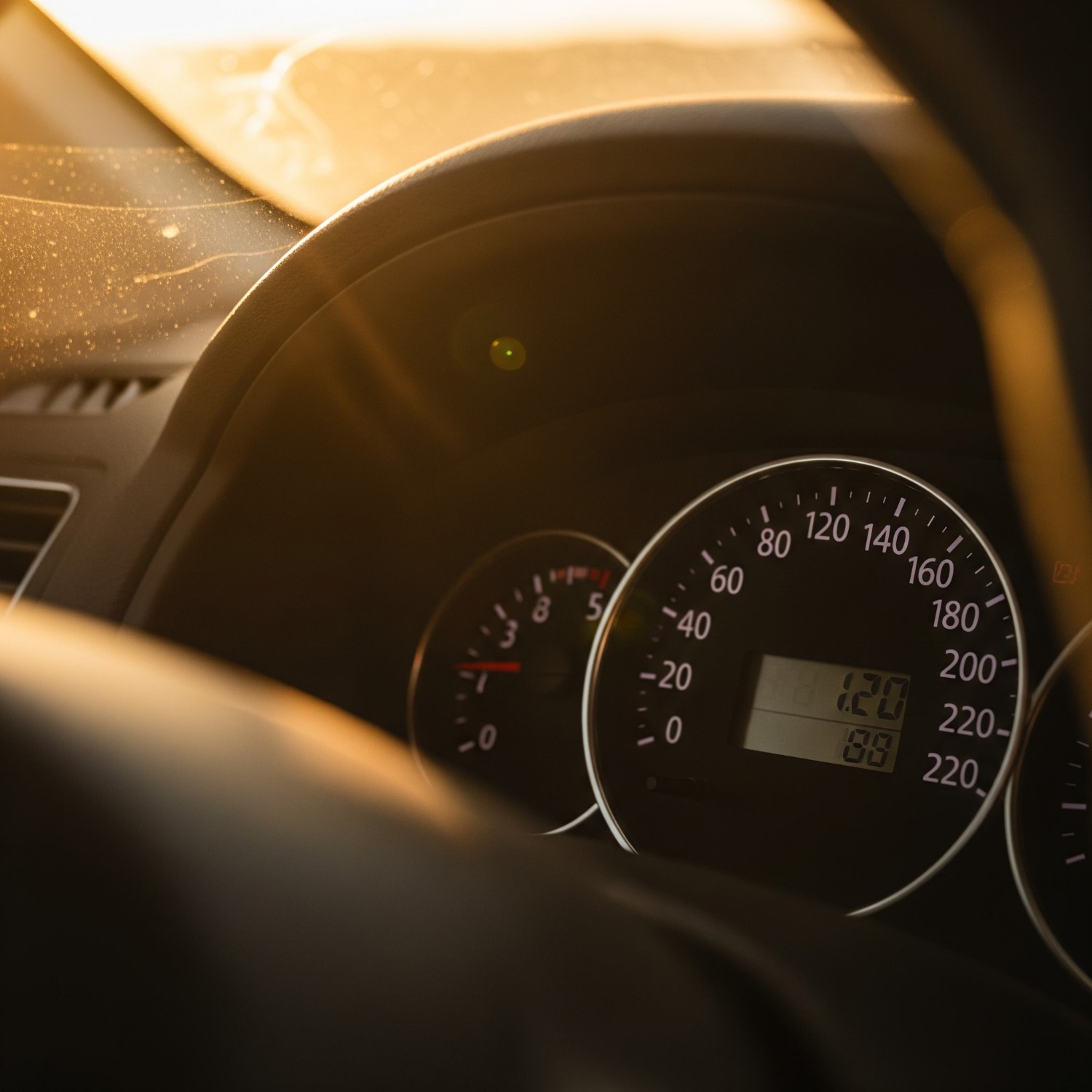 Close-up of a car dashboard speedometer and mileage counter in warm sunset light.